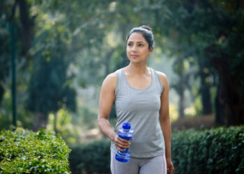 Fit woman running in sportswear with dumbbell shape water bottle at park