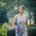 Fit woman running in sportswear with dumbbell shape water bottle at park