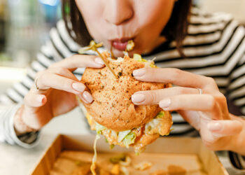 Woman eating a hamburger in modern fastfood cafe, lunch concept