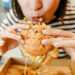 Woman eating a hamburger in modern fastfood cafe, lunch concept