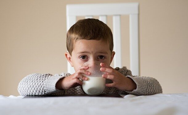 Colour image of a three and a half year old boy sitting at dinner table drinking a glass of whole milk. One of a series.