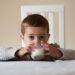 Colour image of a three and a half year old boy sitting at dinner table drinking a glass of whole milk. One of a series.