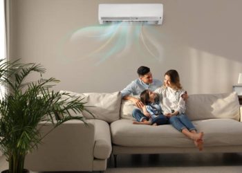 Happy family resting under air conditioner on beige wall at home